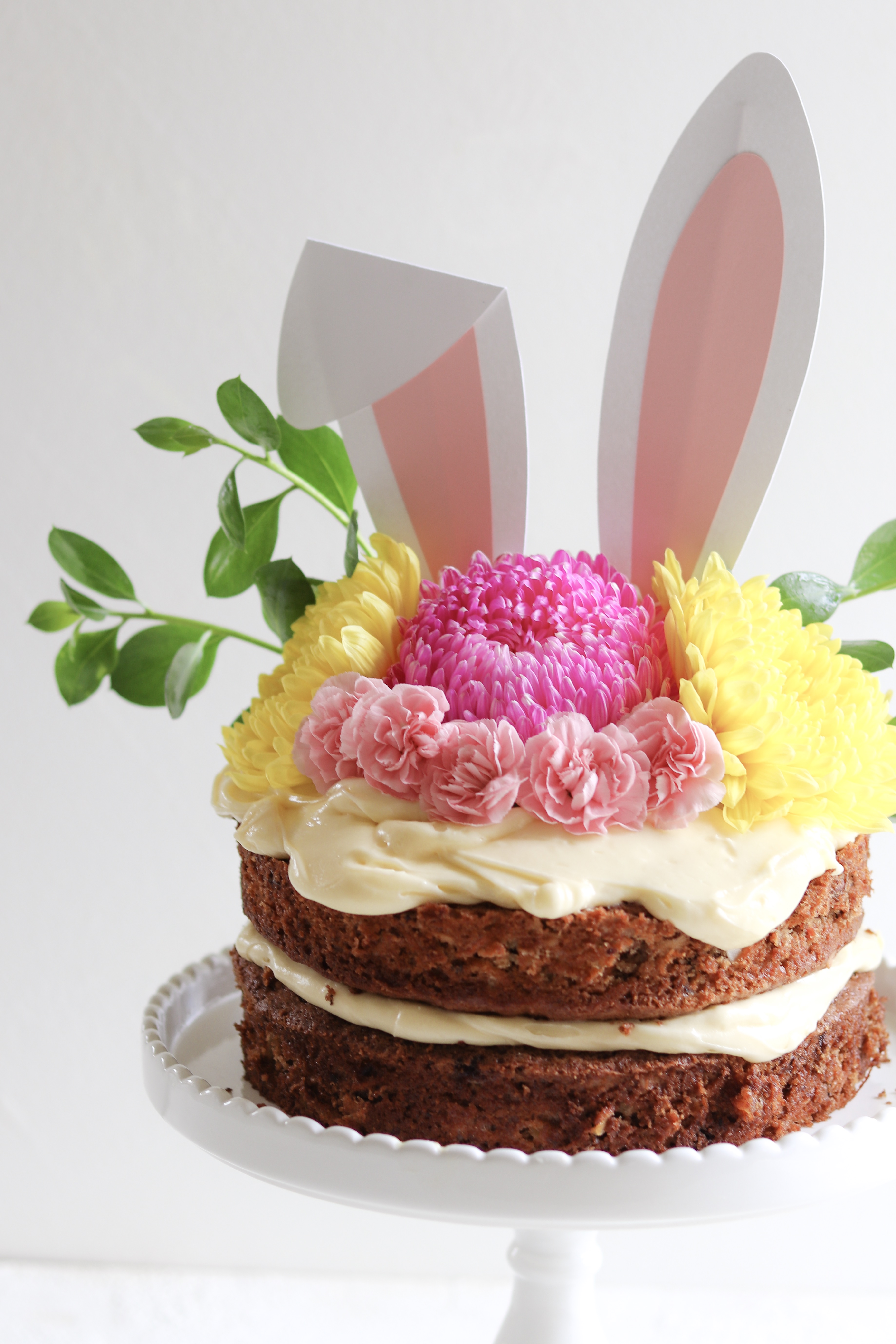 A delicious carrot cake with lashings of cream cheese frosting, decorated for Easter with flowers and bunny ears