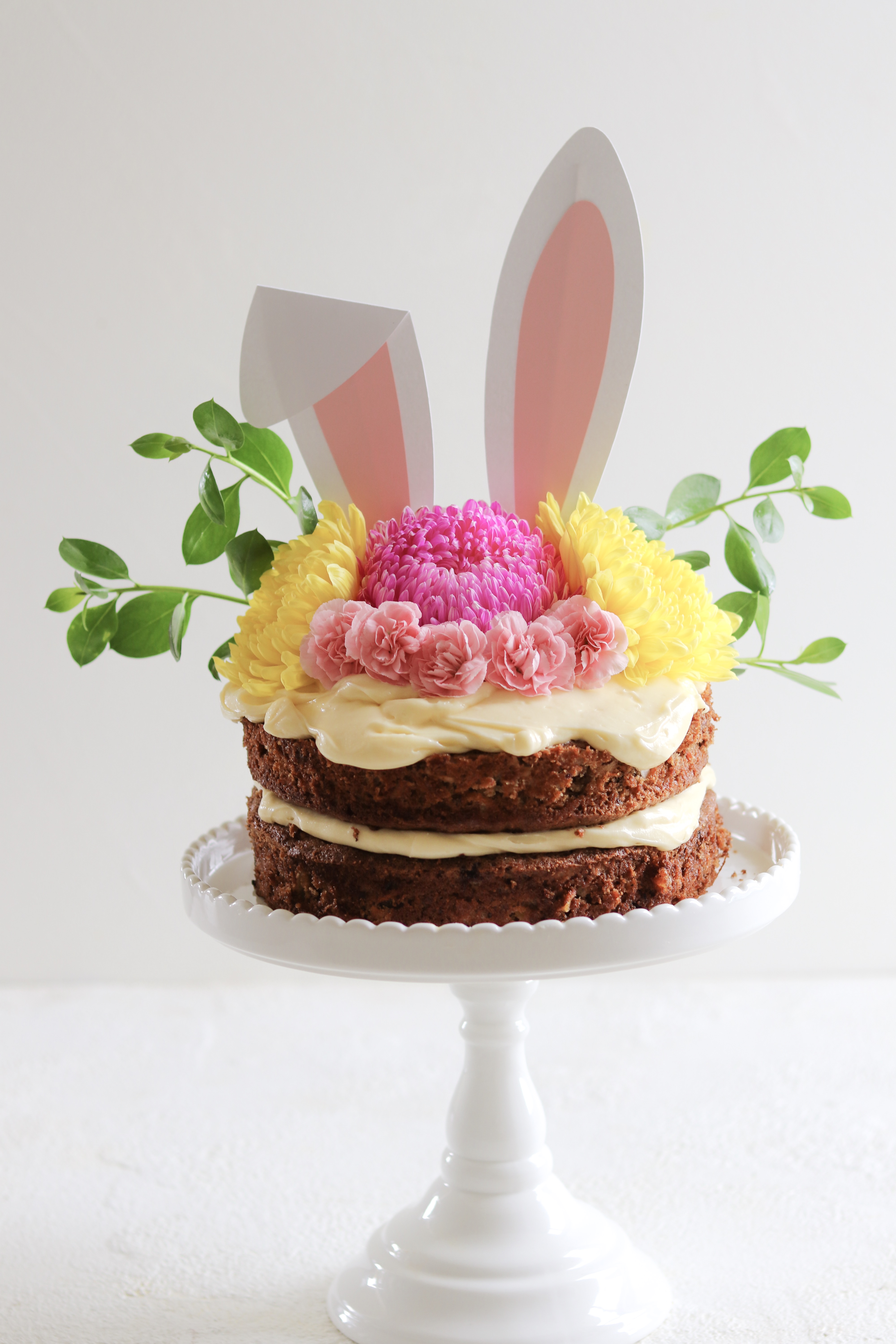 A delicious carrot cake with lashings of cream cheese frosting, decorated for Easter with flowers and bunny ears
