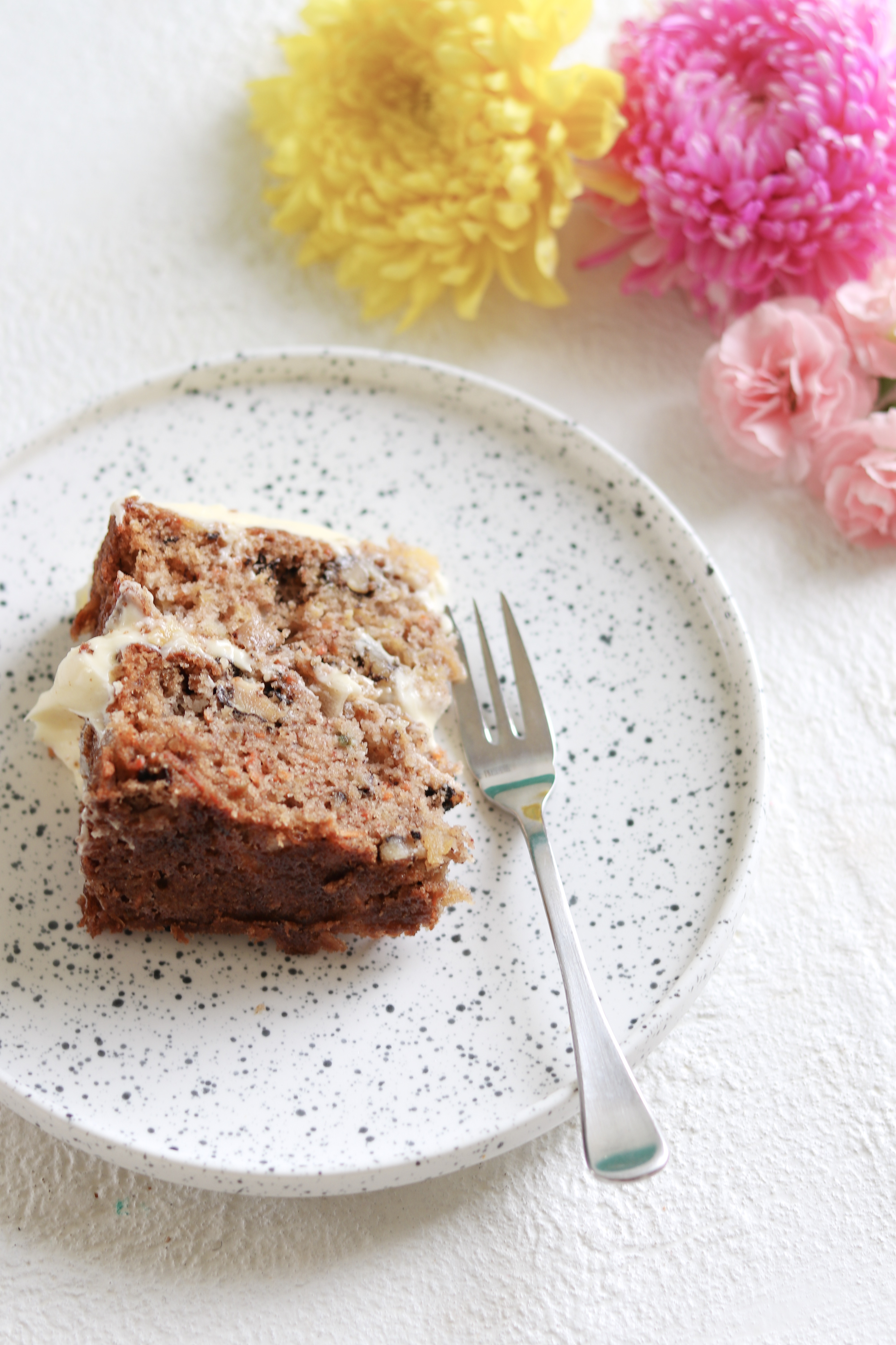 A delicious slice of carrot cake with lashings of cream cheese frosting, on a plate with a fork